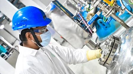 Plant operator in a blue hard hat and mask adjusting reactor equipment during process optimization